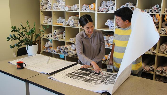 two planners examining a set of paper plans on a large table
