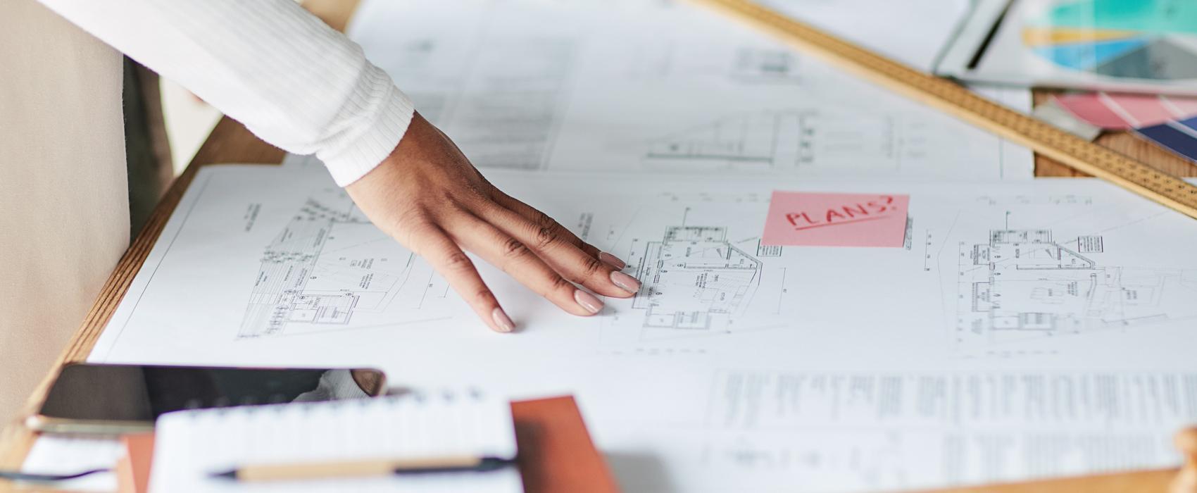 woman's hand runs over architectural plans laying on a desk