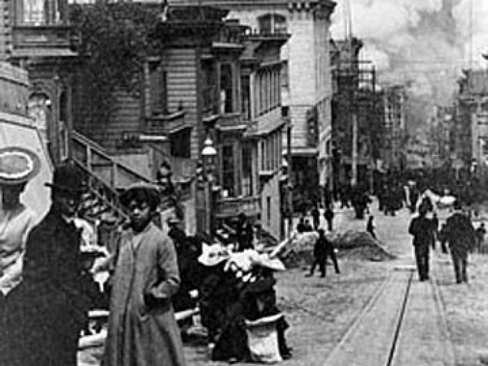 Historic black-and-white photograph showing people standing amid rubble and ruined buildings after the 1906 San Francisco earthquake.