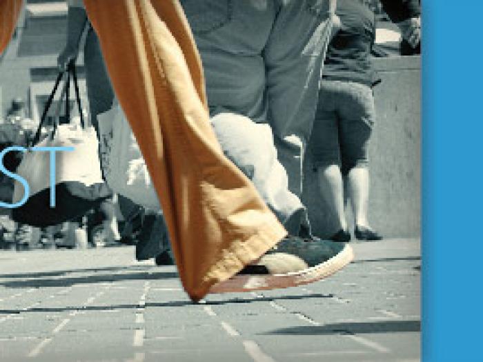 A horizontal banner for WalkFirst featuring a black and white photograph of people's legs and feet walking across a city street with the word WALKFIRST in bold white letters, next to a blue block of text that reads A framework for pedestrian improvements in San Francisco.
