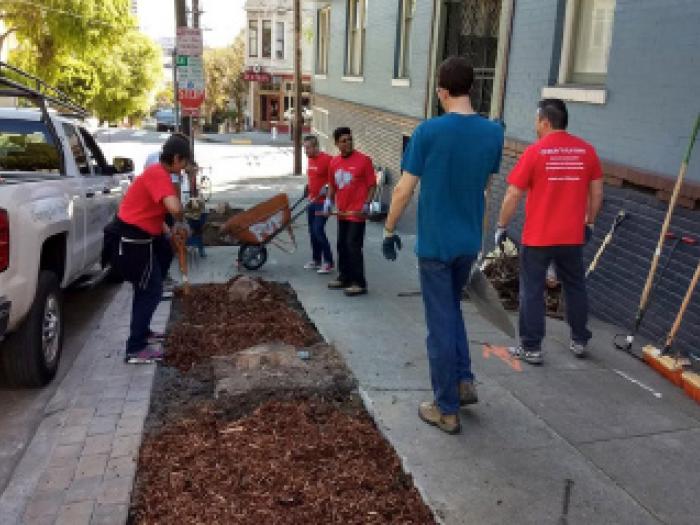 A candid photo of several people standing on a city sidewalk next to a building with a large glass storefront.