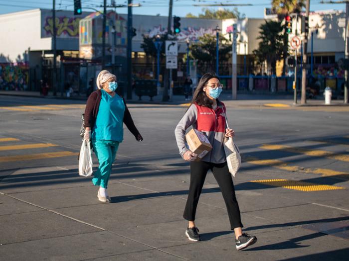 Two women wearing protective masks walking at crosswalk on 16th Street in the Mission District