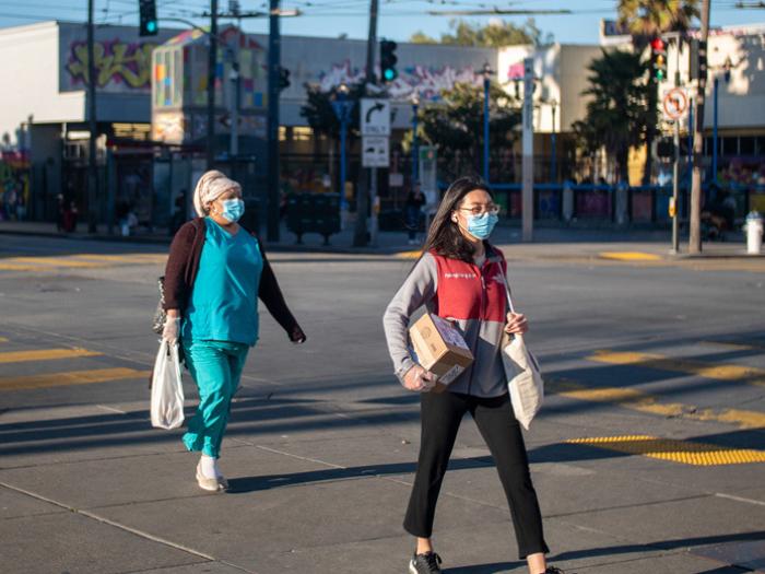 Two women wearing protective masks walking at crosswalk on 16th Street in the Mission District