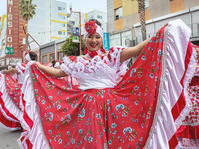 A dancer in a vibrant red, white, and floral folkloric dress performing at San Francisco Carnaval in the Mission District.